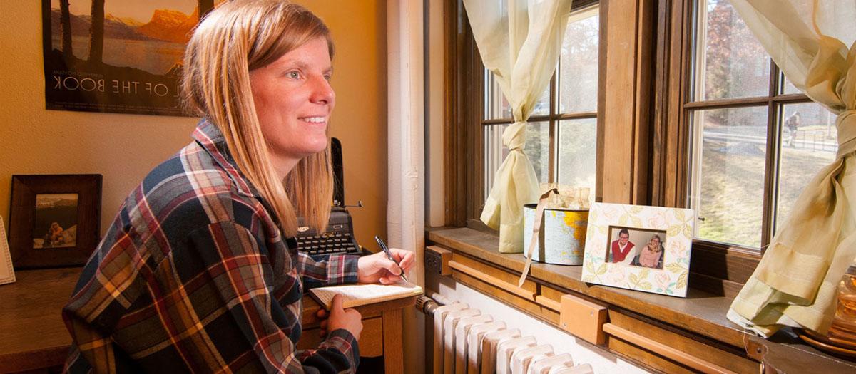 A graduate student writing at her desk in Brink Hall