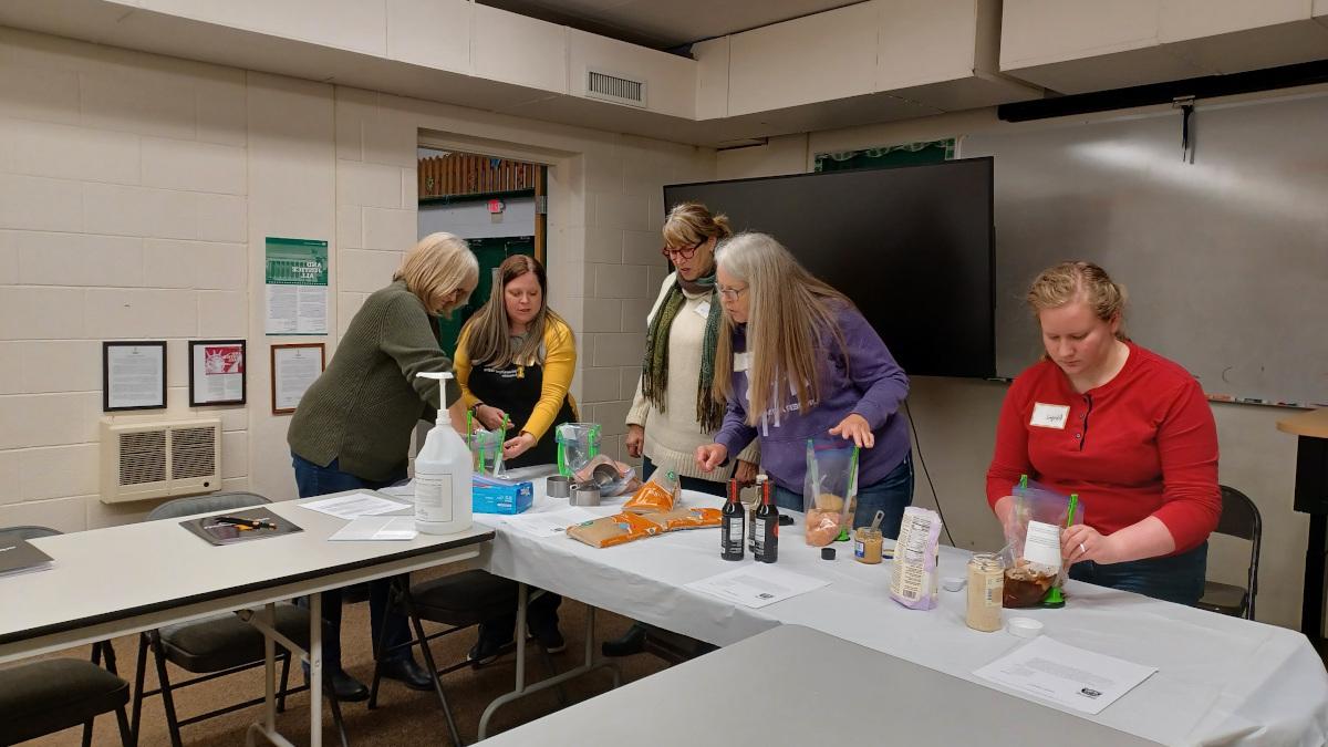 Adults prepare meals in a classroom environment.